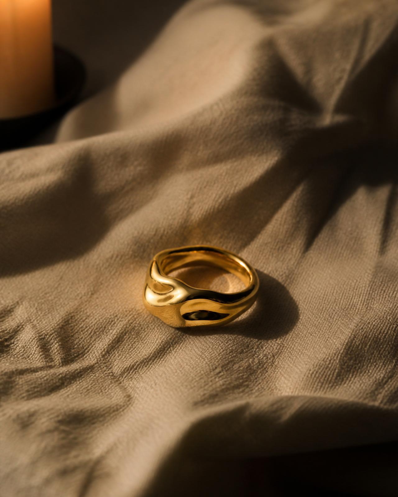 A single sculptural gold ring resting in candlelight